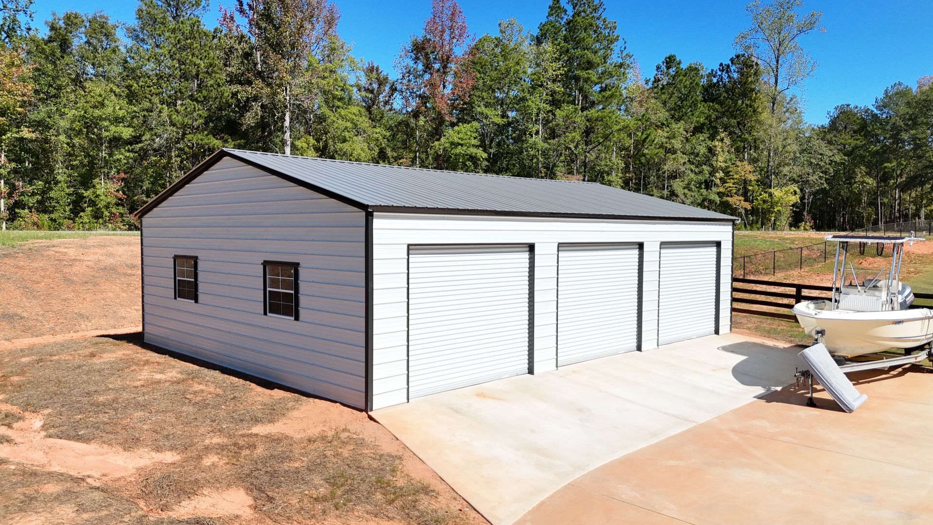 A white garage with three doors and a boat parked in front of it.