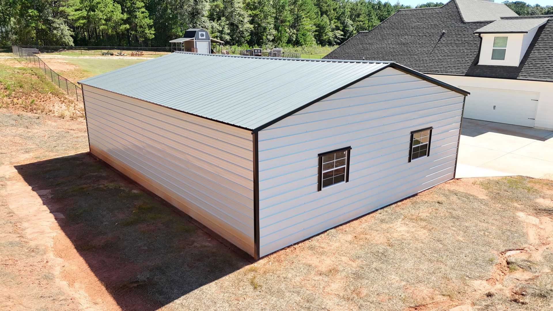 A white building with a metal roof is sitting in the middle of a dirt field.