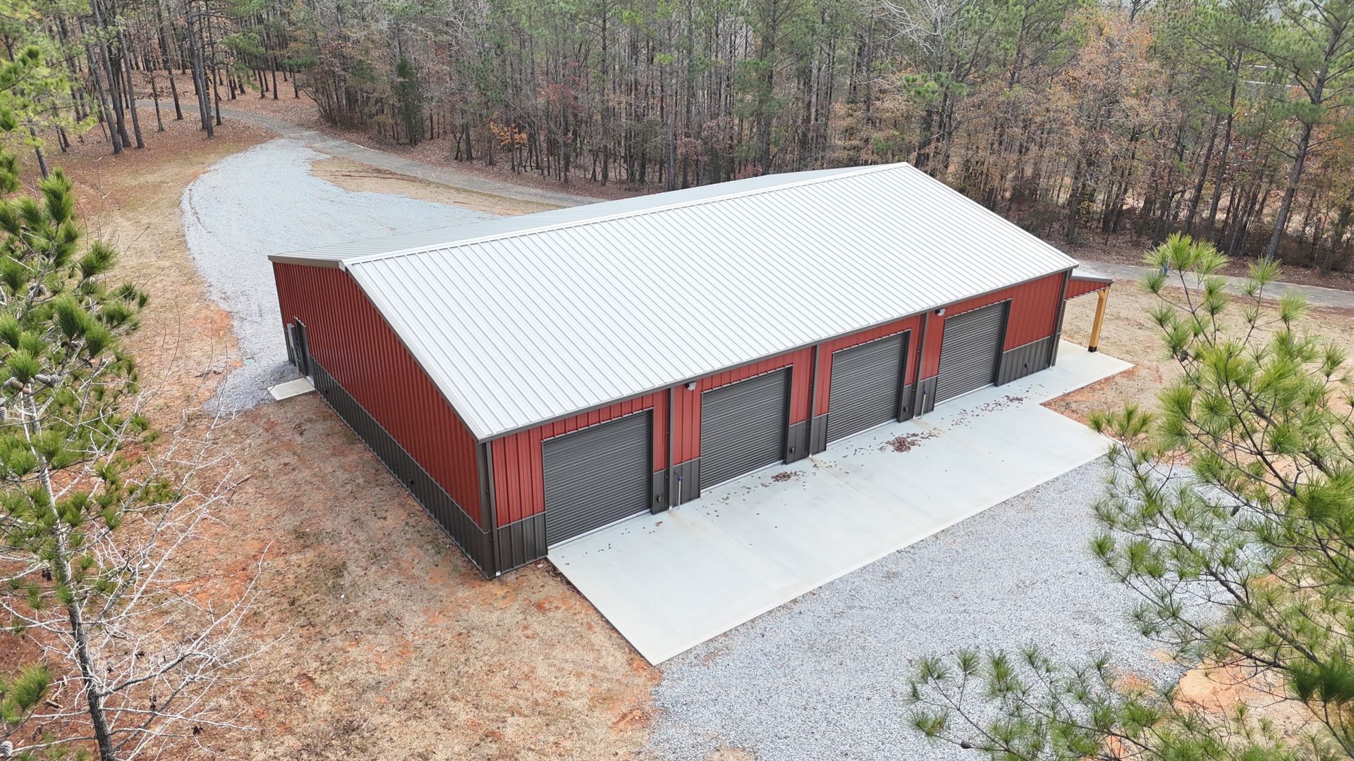 An aerial view of a red barn with a white roof and a driveway surrounded by trees.