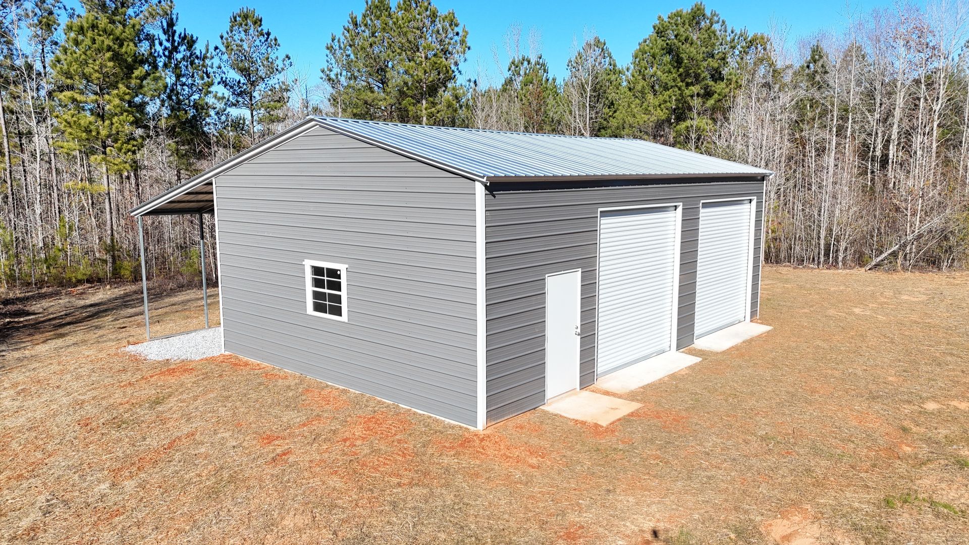 A metal garage with two garage doors is sitting in the middle of a field.