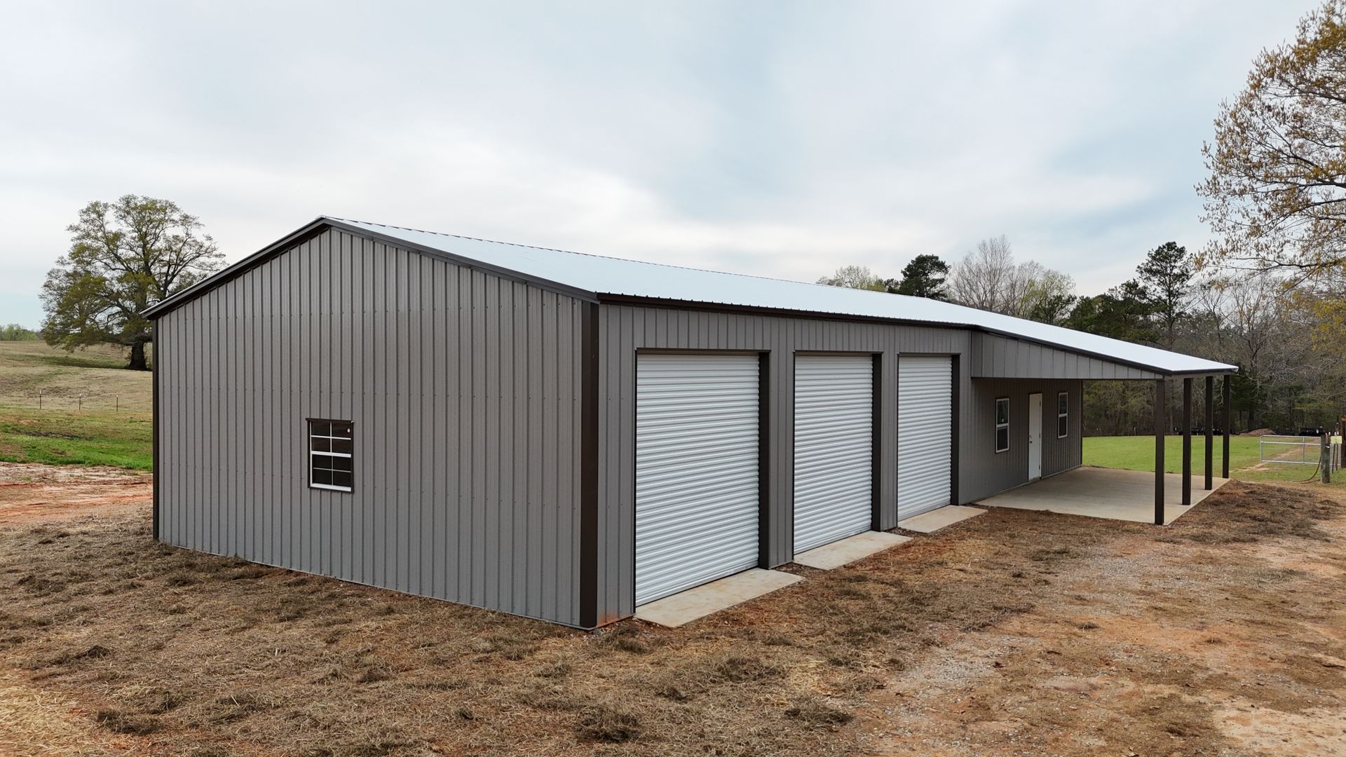 A metal building with three garages and a cover on top of a dirt field