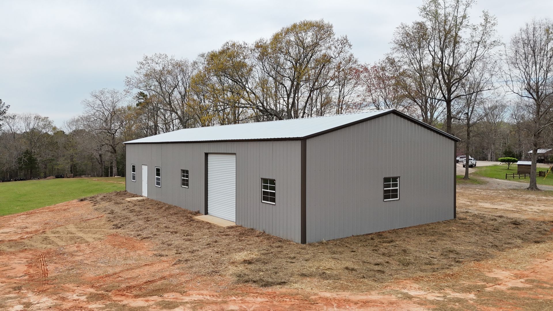 A metal building with three garages and a cover on top of a dirt field