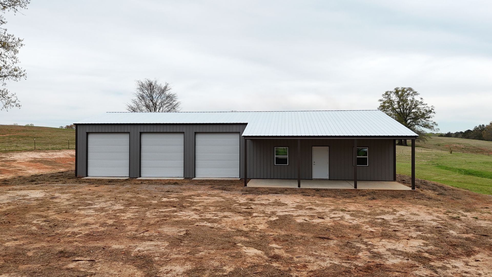 A metal building with three garages and a cover on dirt