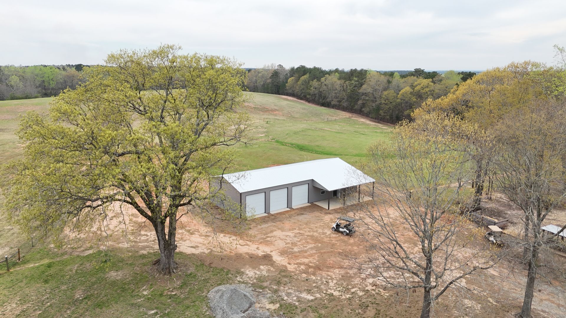 An aerial view of a barn in the middle of a field surrounded by trees.