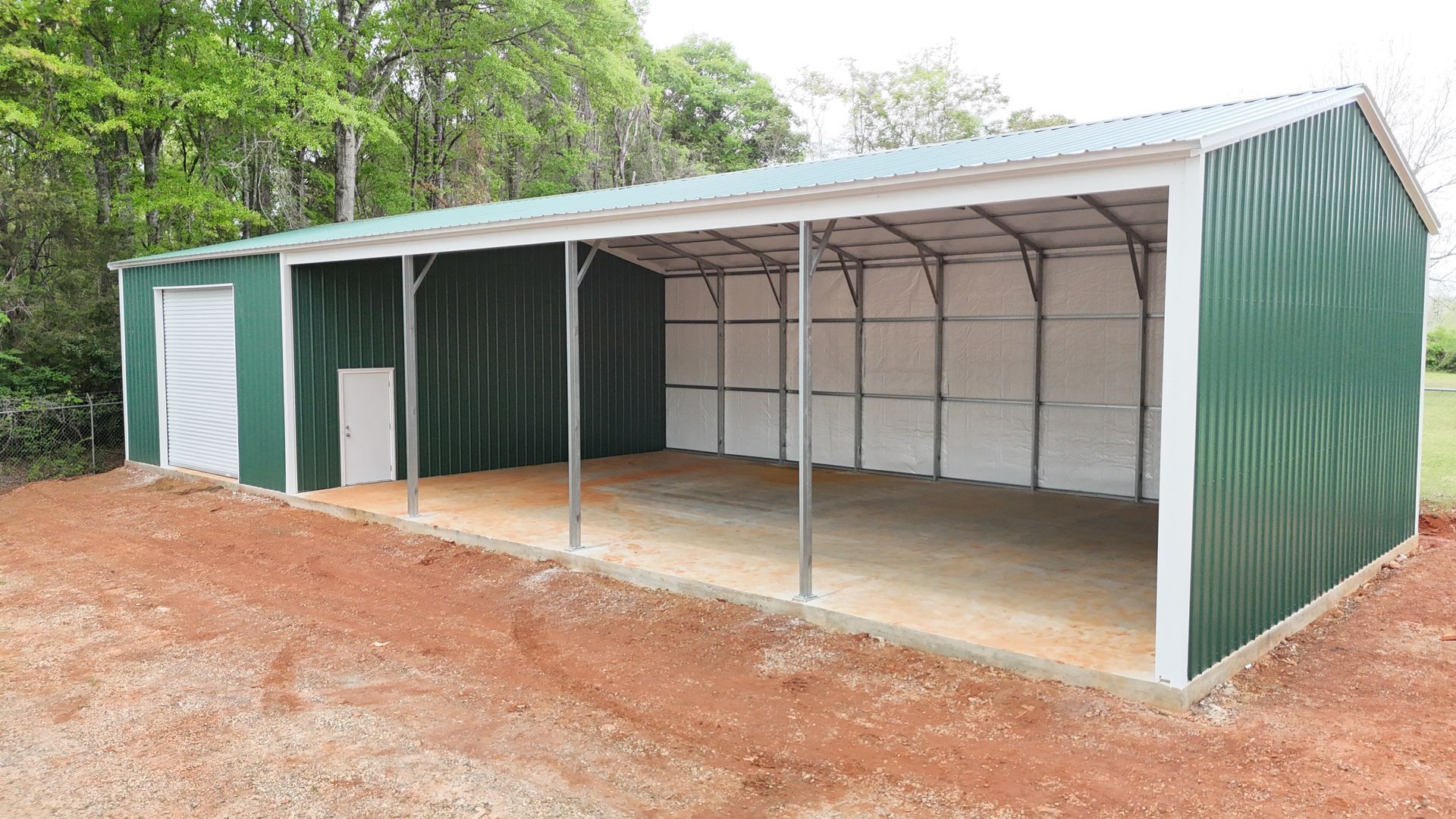 A green and white metal barn is sitting on top of a dirt field.