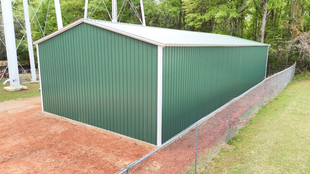 A green metal building is sitting next to a chain link fence.