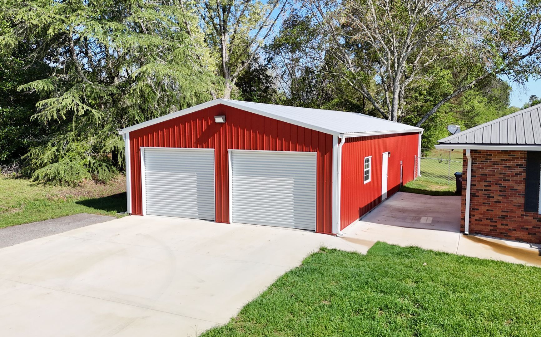 A red garage with two garage doors is next to a brick house.