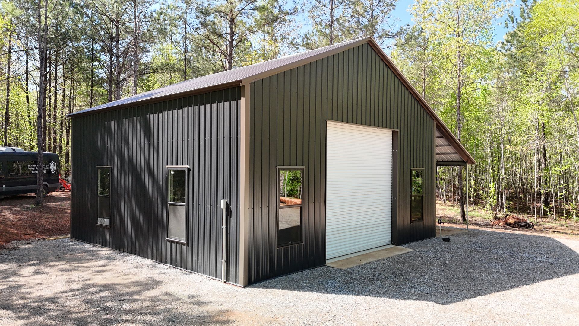 A steel building with one garage and a cover sitting on gravel