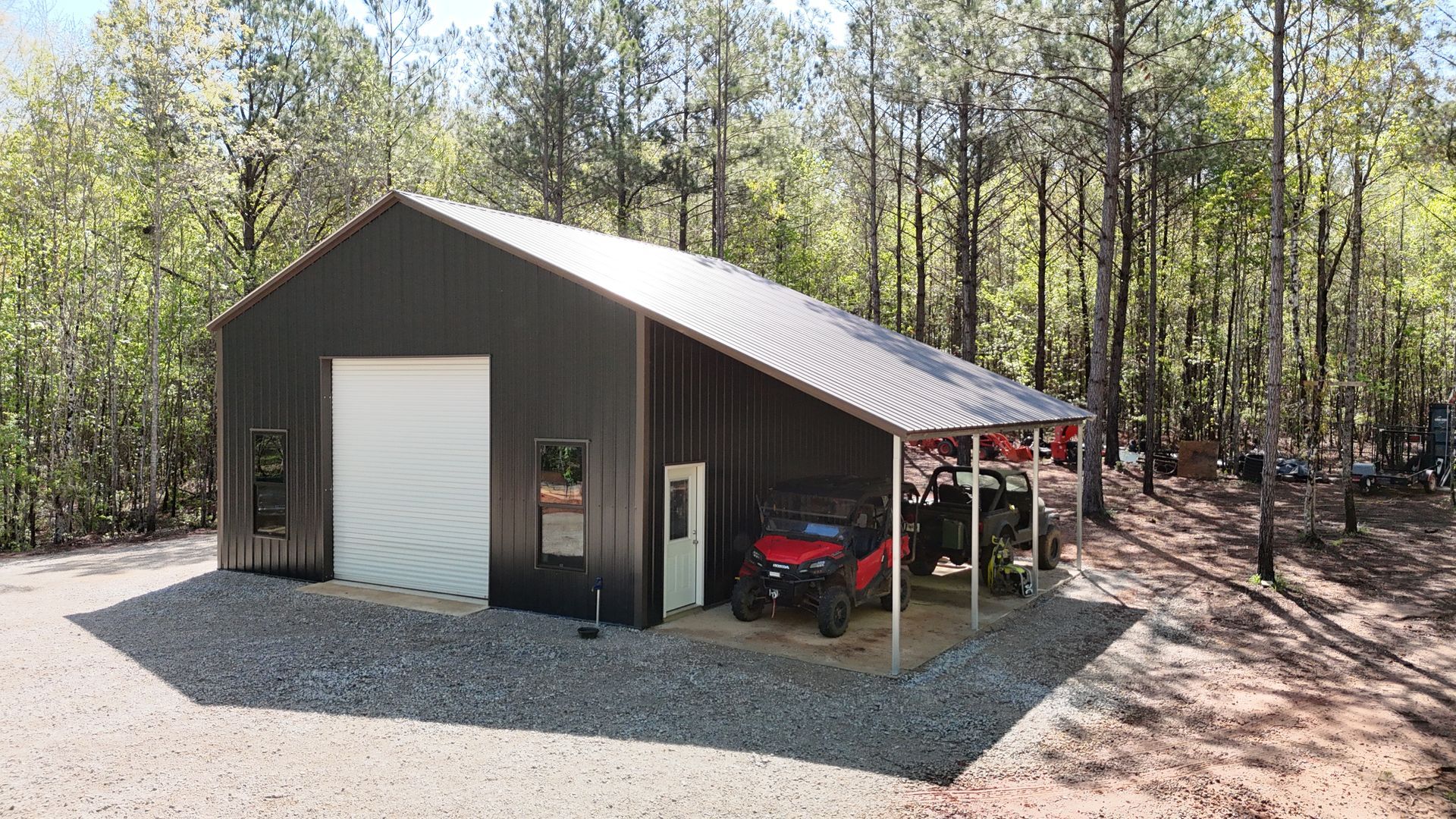 A metal building with one garage and a cover sitting on gravel
