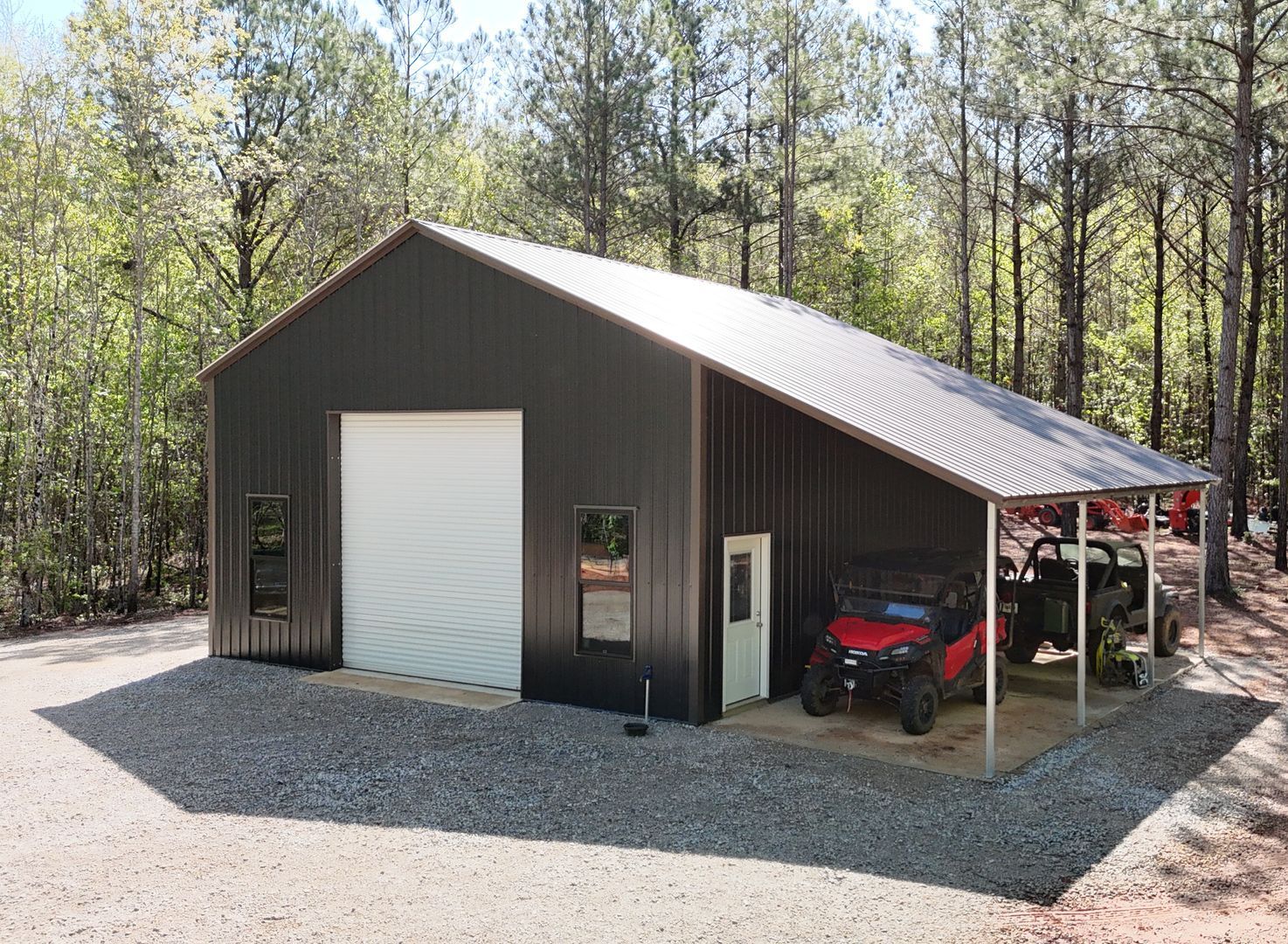 A large metal building with a black roof is sitting in the middle of a field.