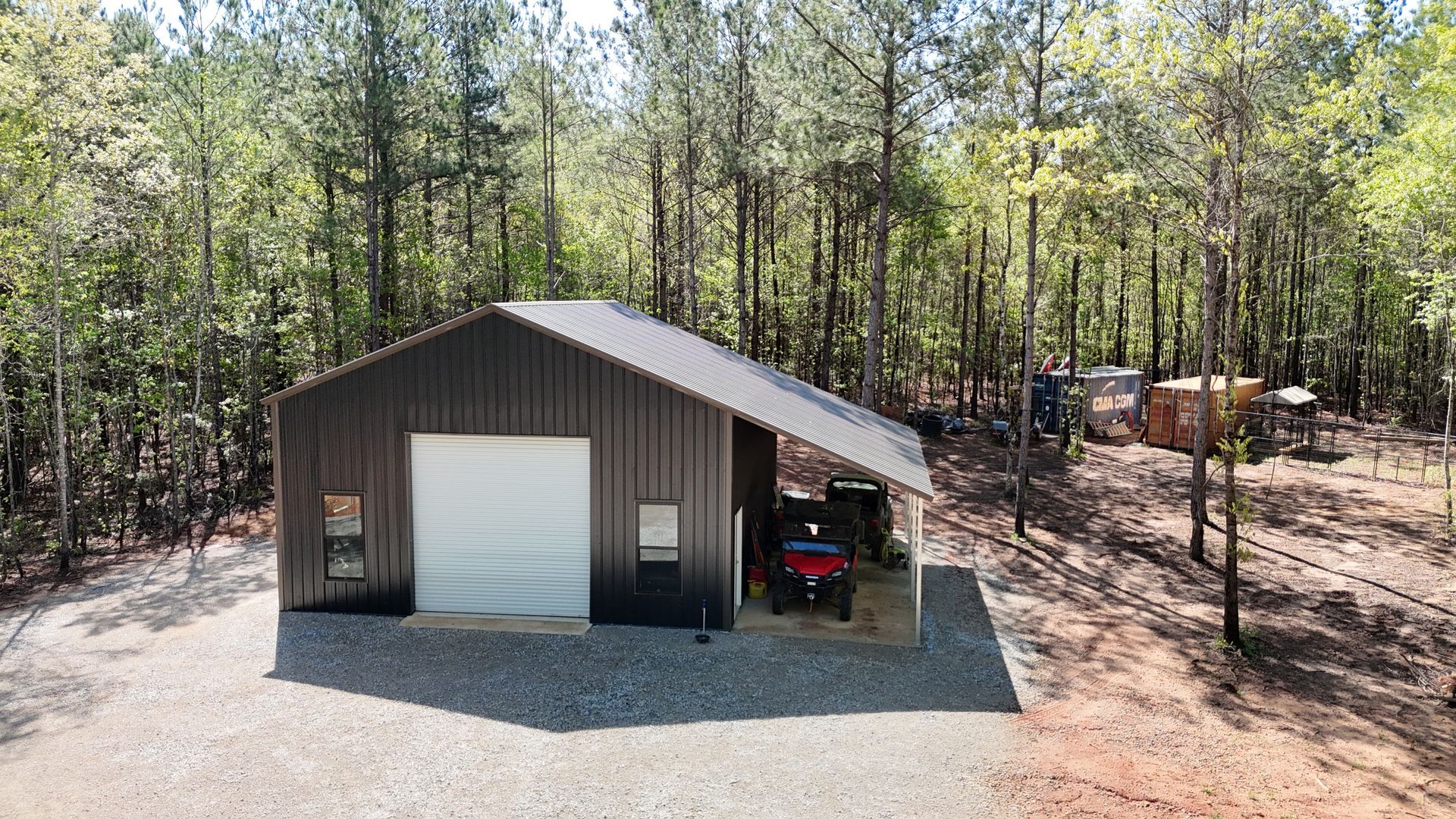 A steel building with one garage and a cover sitting on gravel