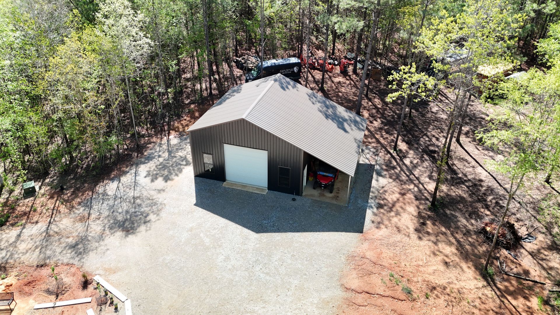 A steel building with one garage and a cover sitting on gravel