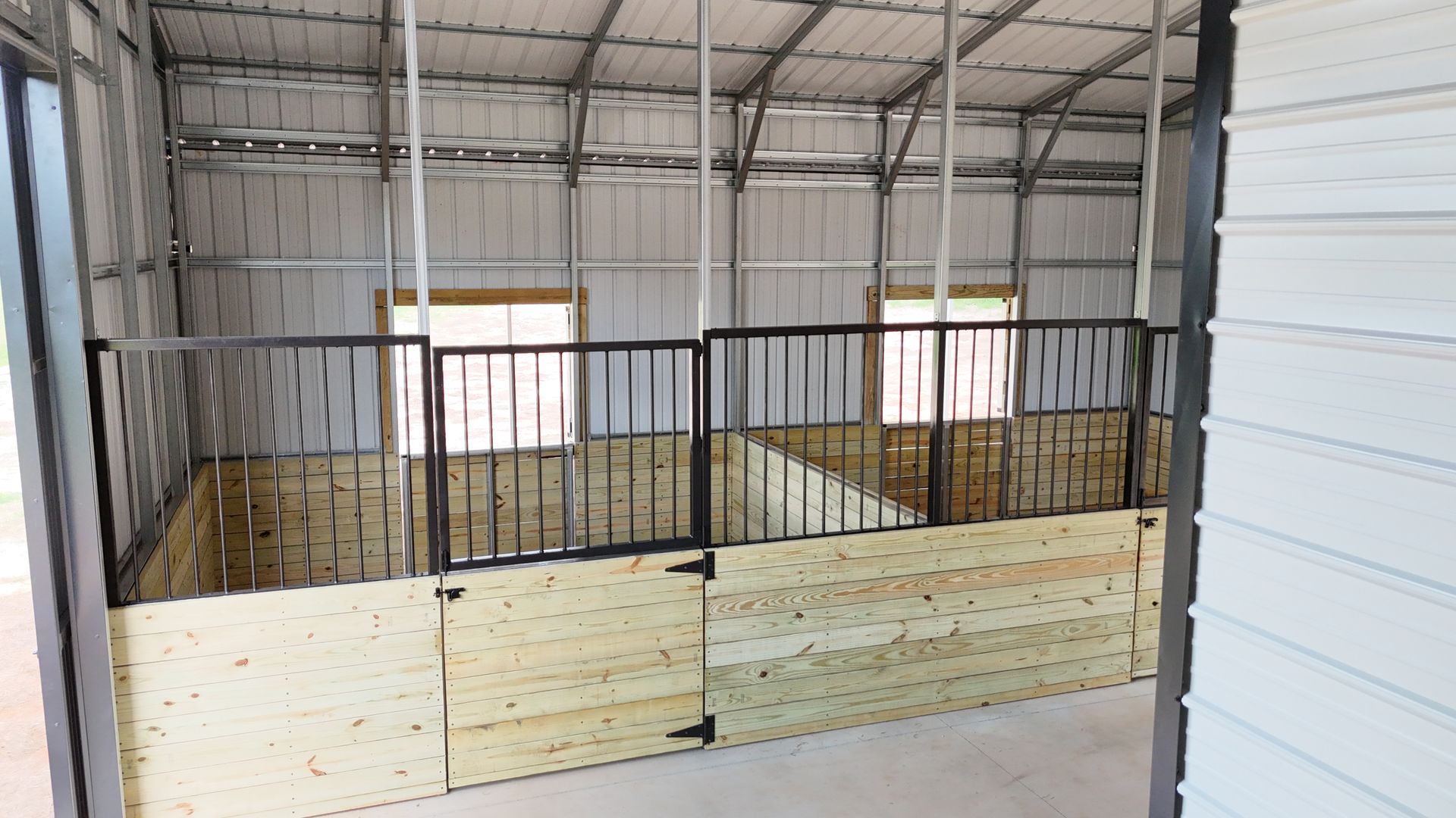 The inside of a barn with wooden stalls and a metal roof.