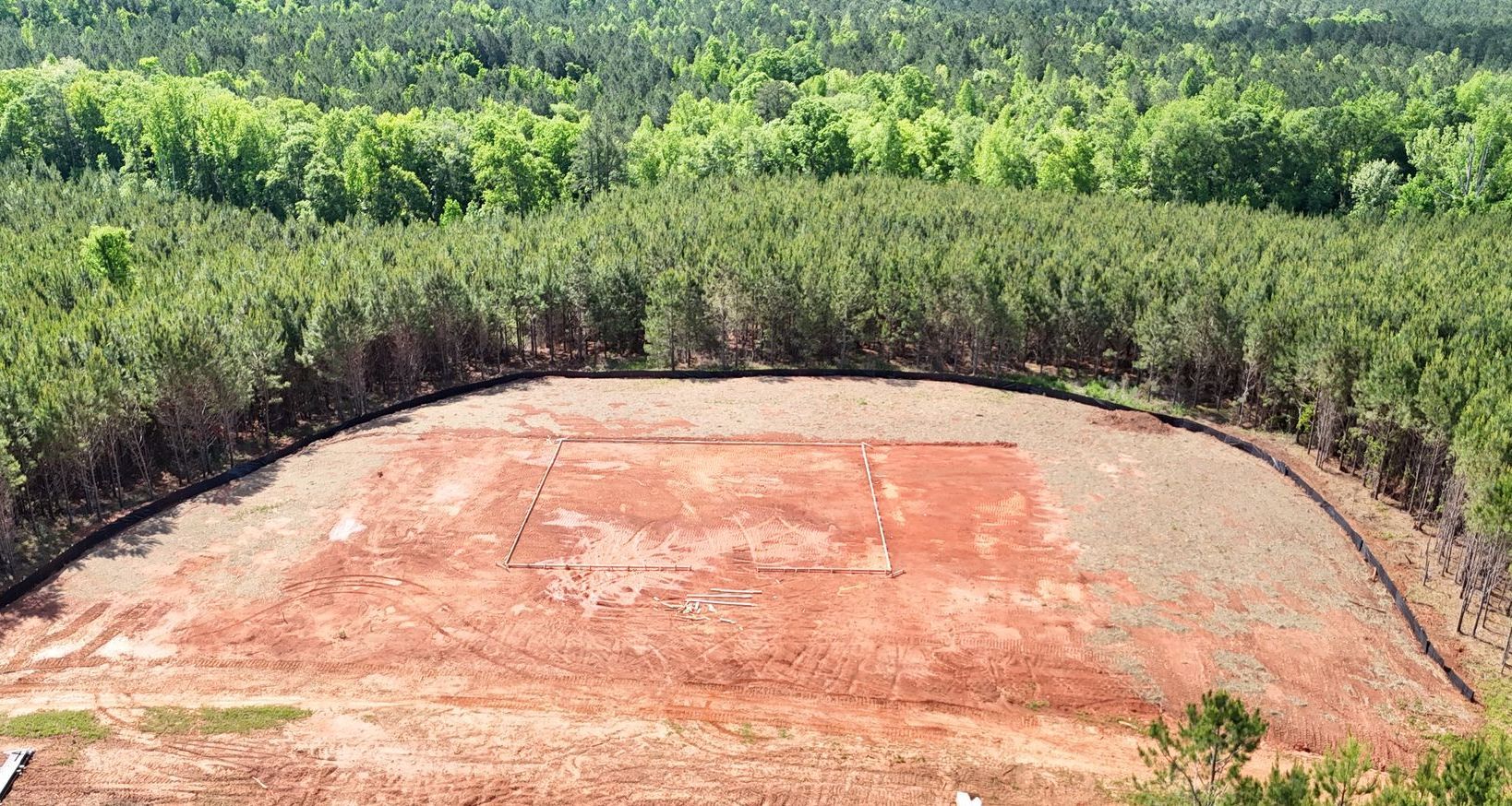 An aerial view of a dirt field surrounded by trees.