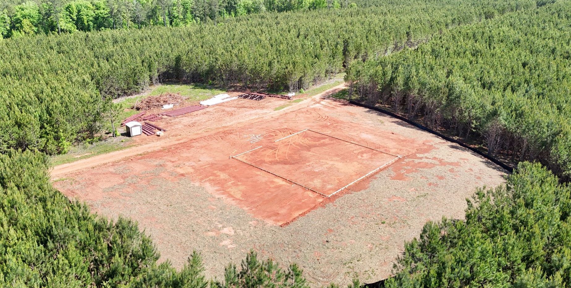 An aerial view of a dirt field surrounded by trees.
