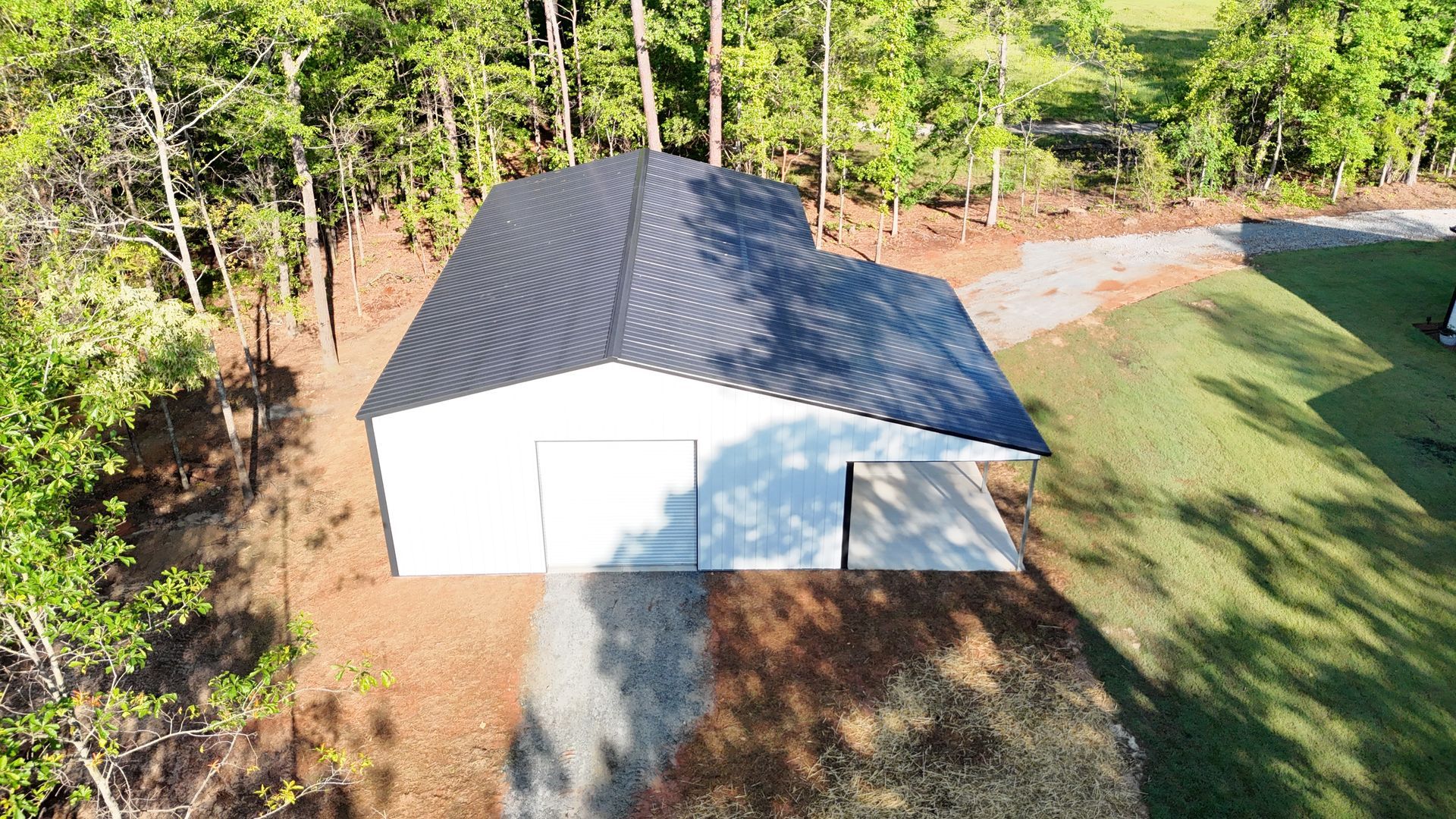 An aerial view of a white garage with a black roof surrounded by trees.