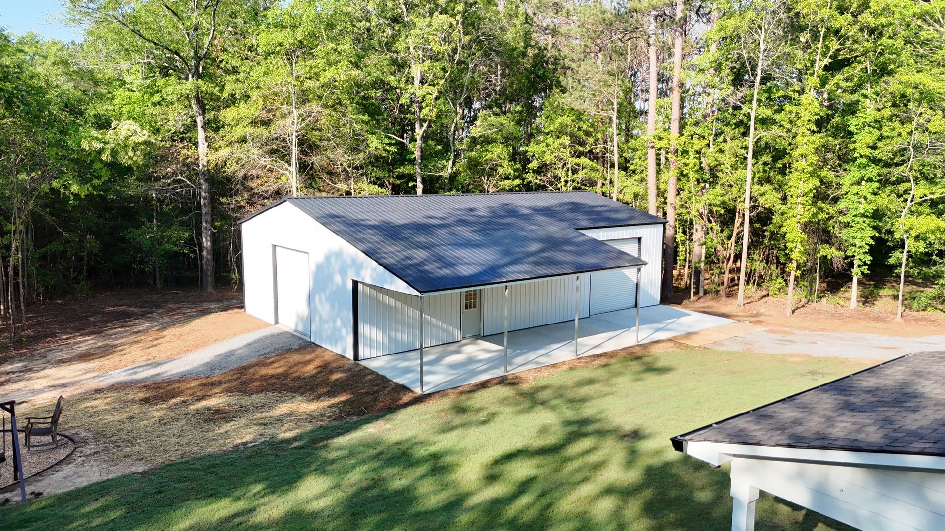 A white garage with a black roof is surrounded by trees.