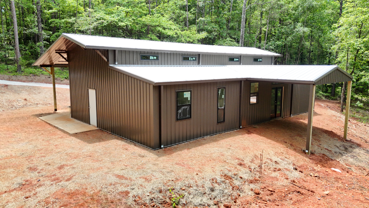 A large metal building with a white roof is sitting in the middle of a dirt field.