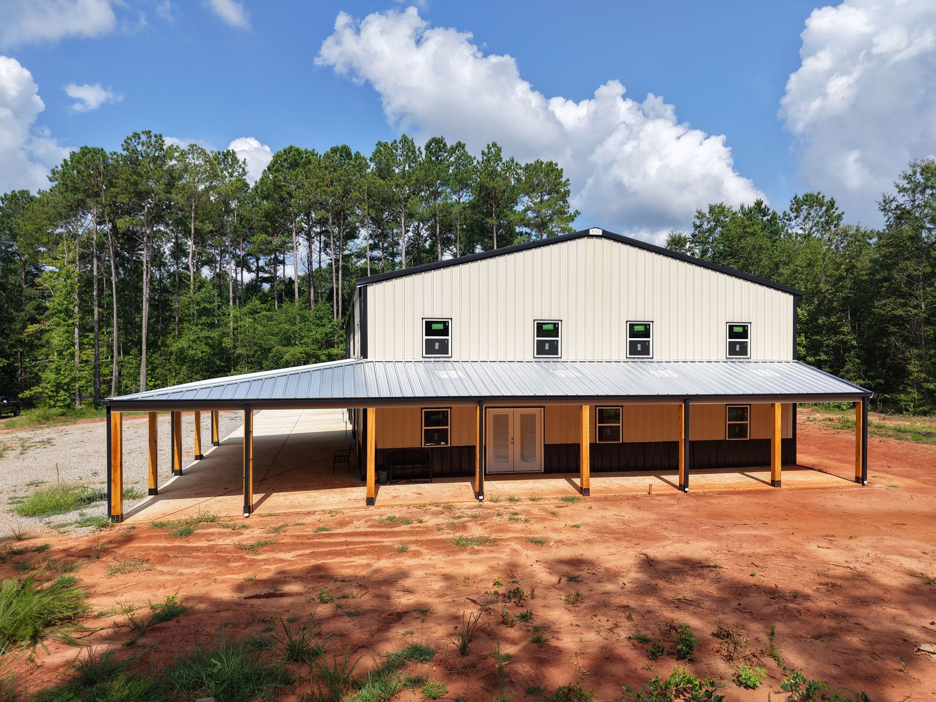 Metal building with a covered porch, set in a clearing with trees and a blue sky.
