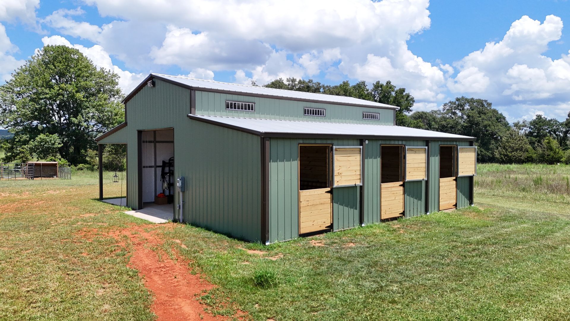 A green barn is sitting in the middle of a grassy field.