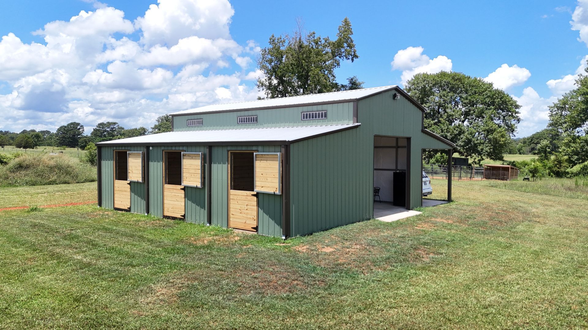 A green barn is sitting in the middle of a grassy field.