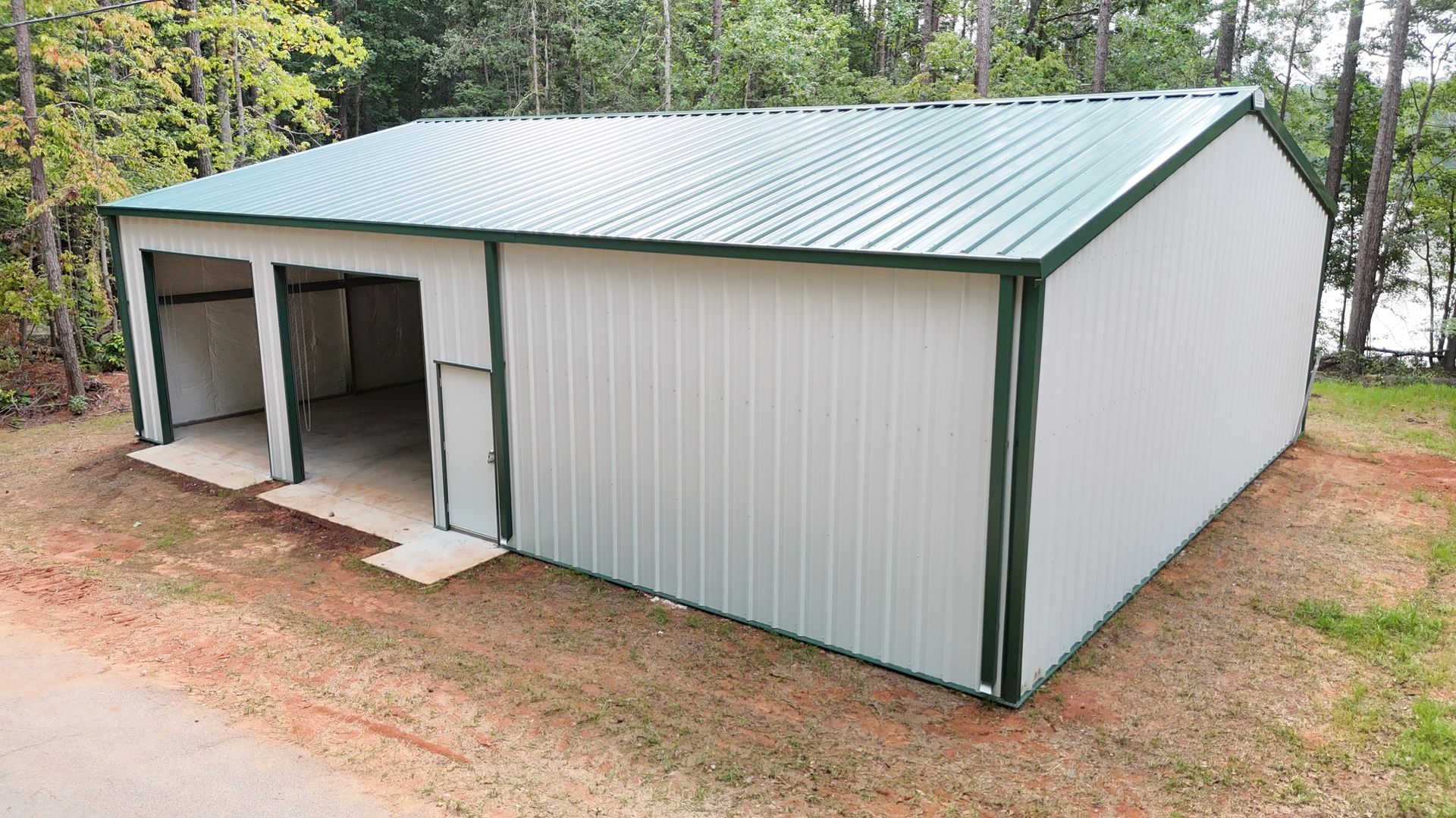 A white metal building with a green roof is sitting on top of a dirt field.