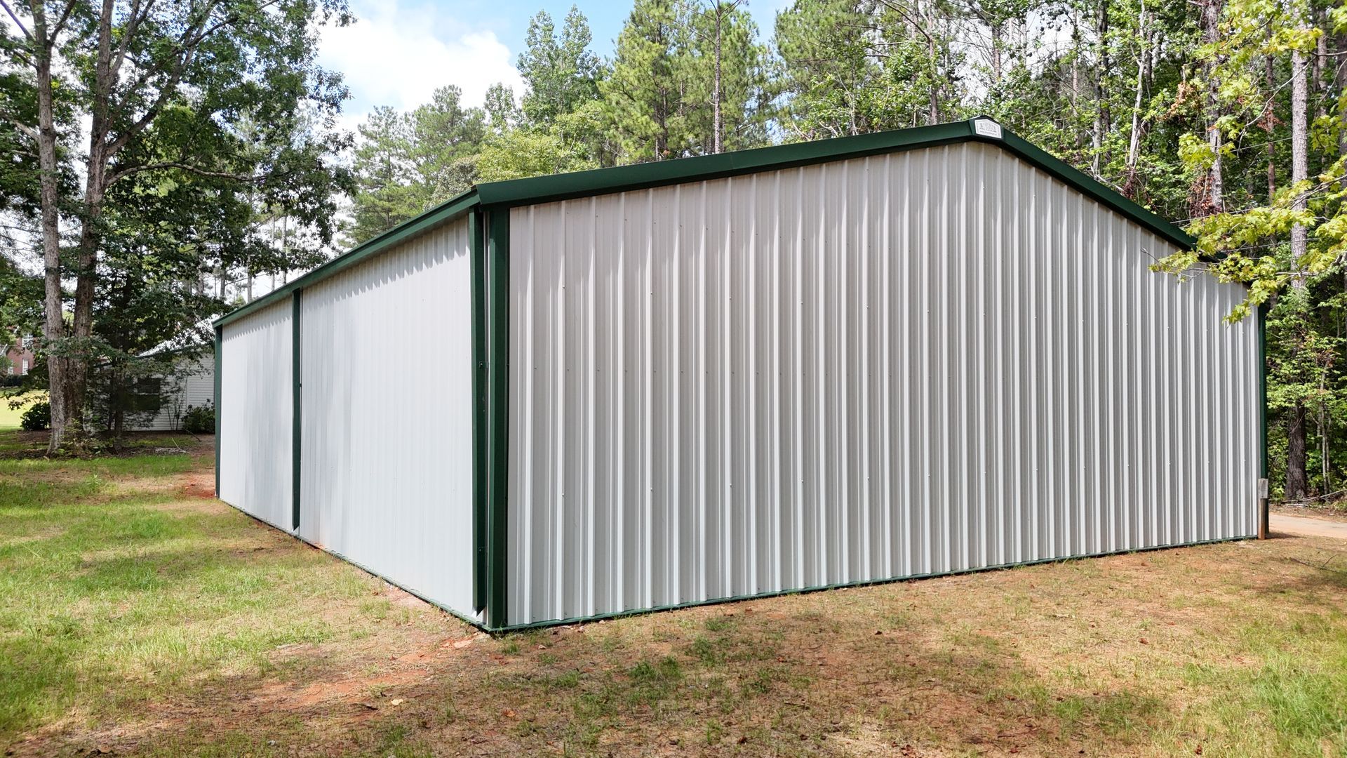 A white metal building with a green roof is sitting in the middle of a grassy field.