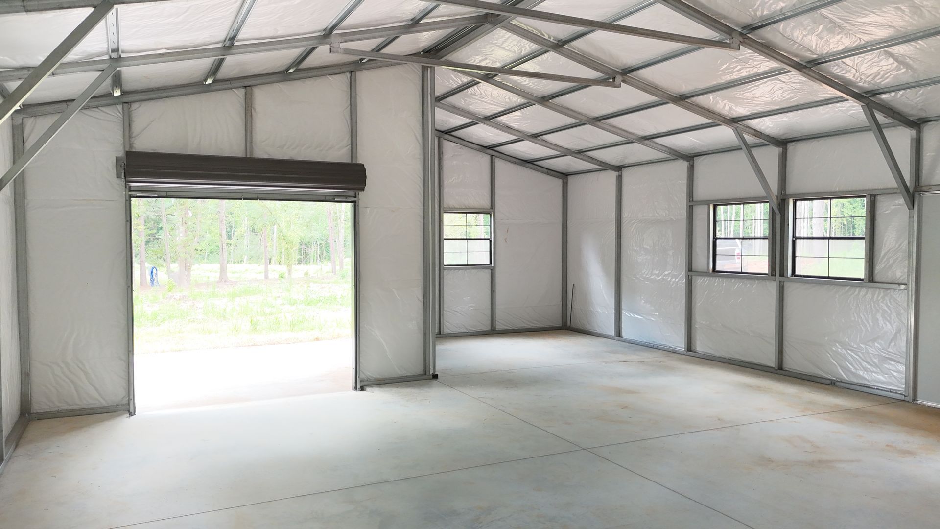 Inside view of an empty metal building with a roll-up door, windows, and a concrete floor.