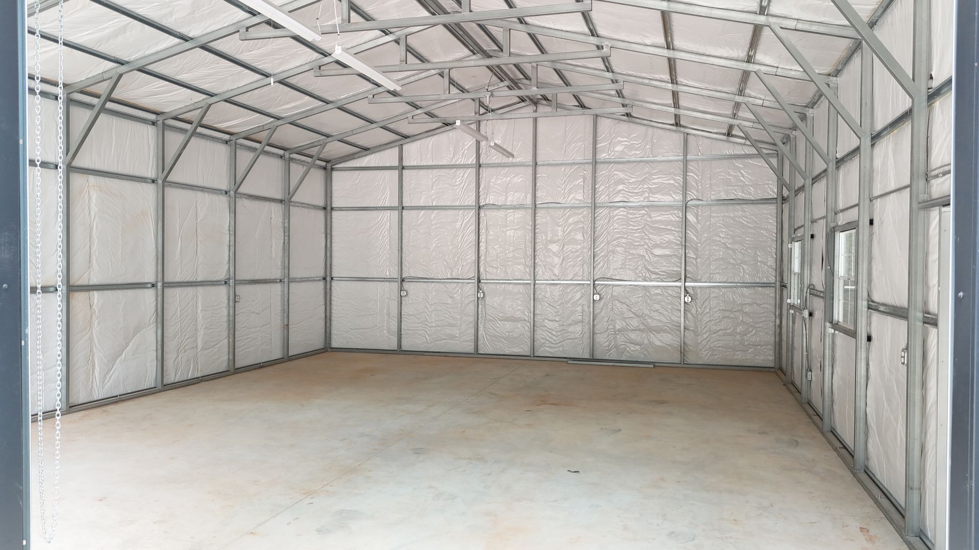 Empty metal-framed storage building with white insulated walls and ceiling. Interior shot with a concrete floor.
