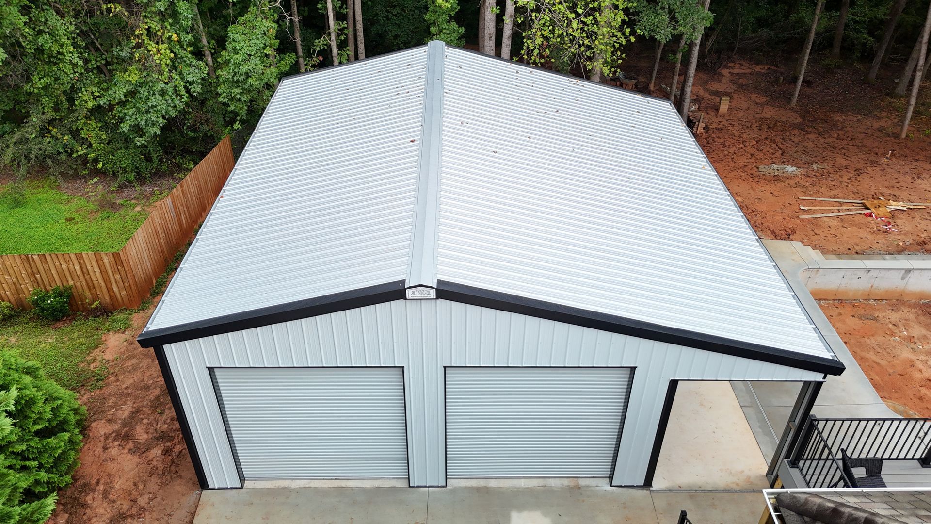 A metal garage with two bays and a curved roof, viewed from above, set in a yard with trees and a driveway.