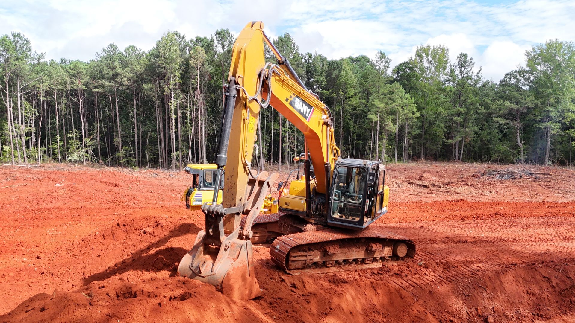 Yellow excavator digging in red earth, with forest in the background.