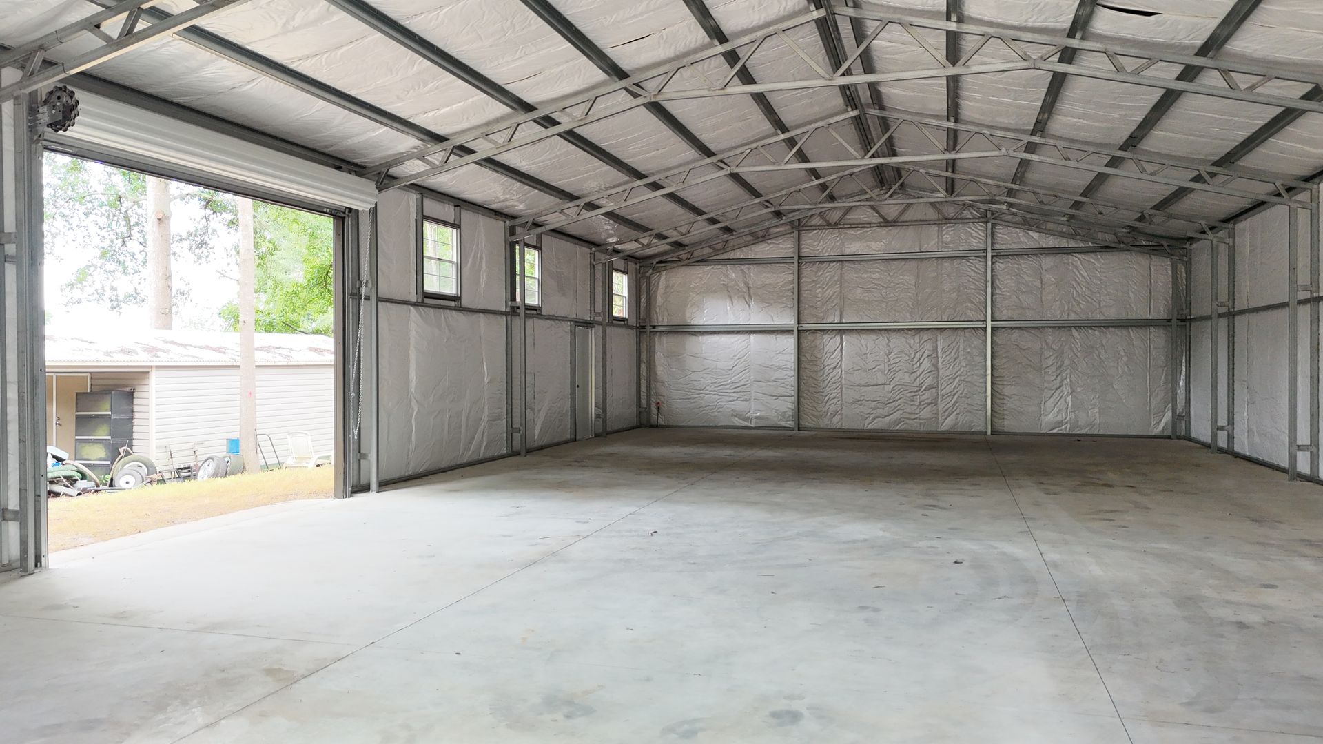 Inside of an empty metal storage building, concrete floor, open door, and small windows.