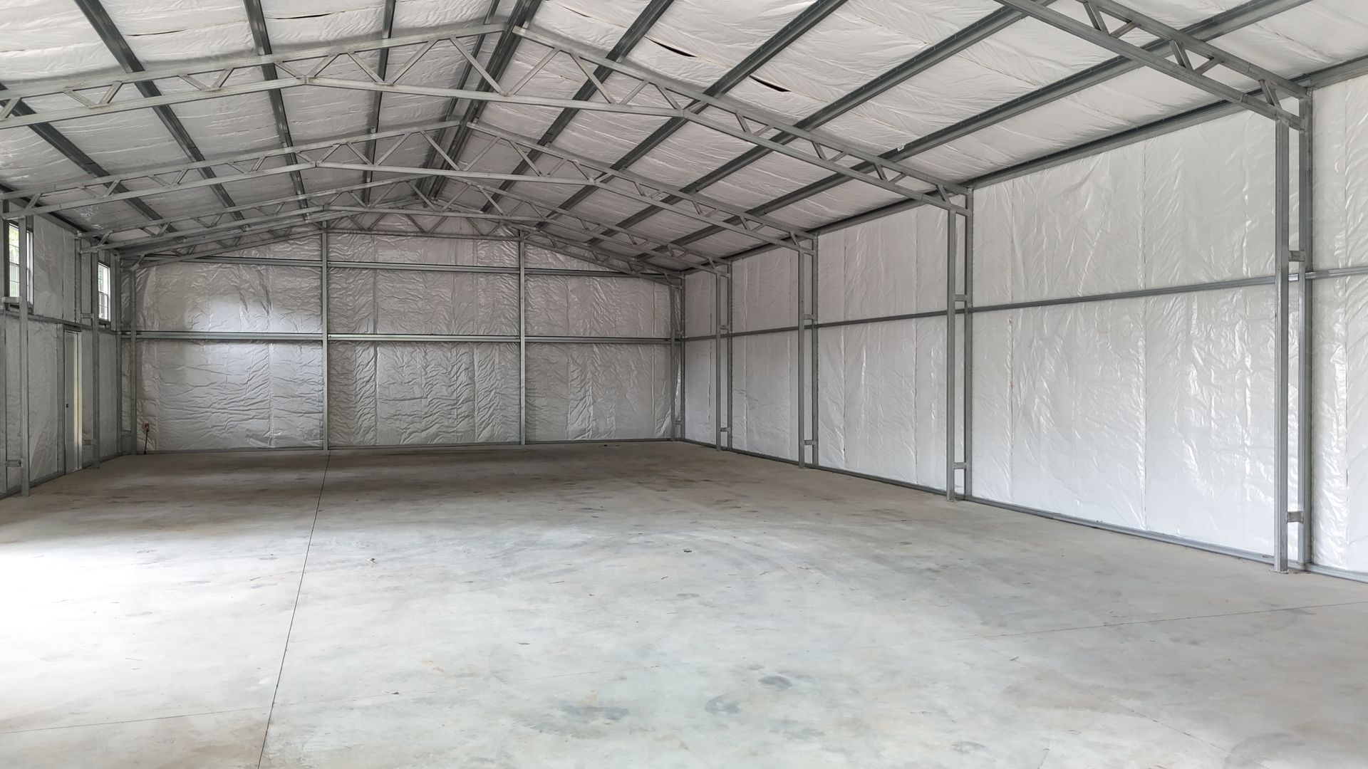 Interior of a large empty metal building with concrete floor, white insulated walls, and gray metal beams.