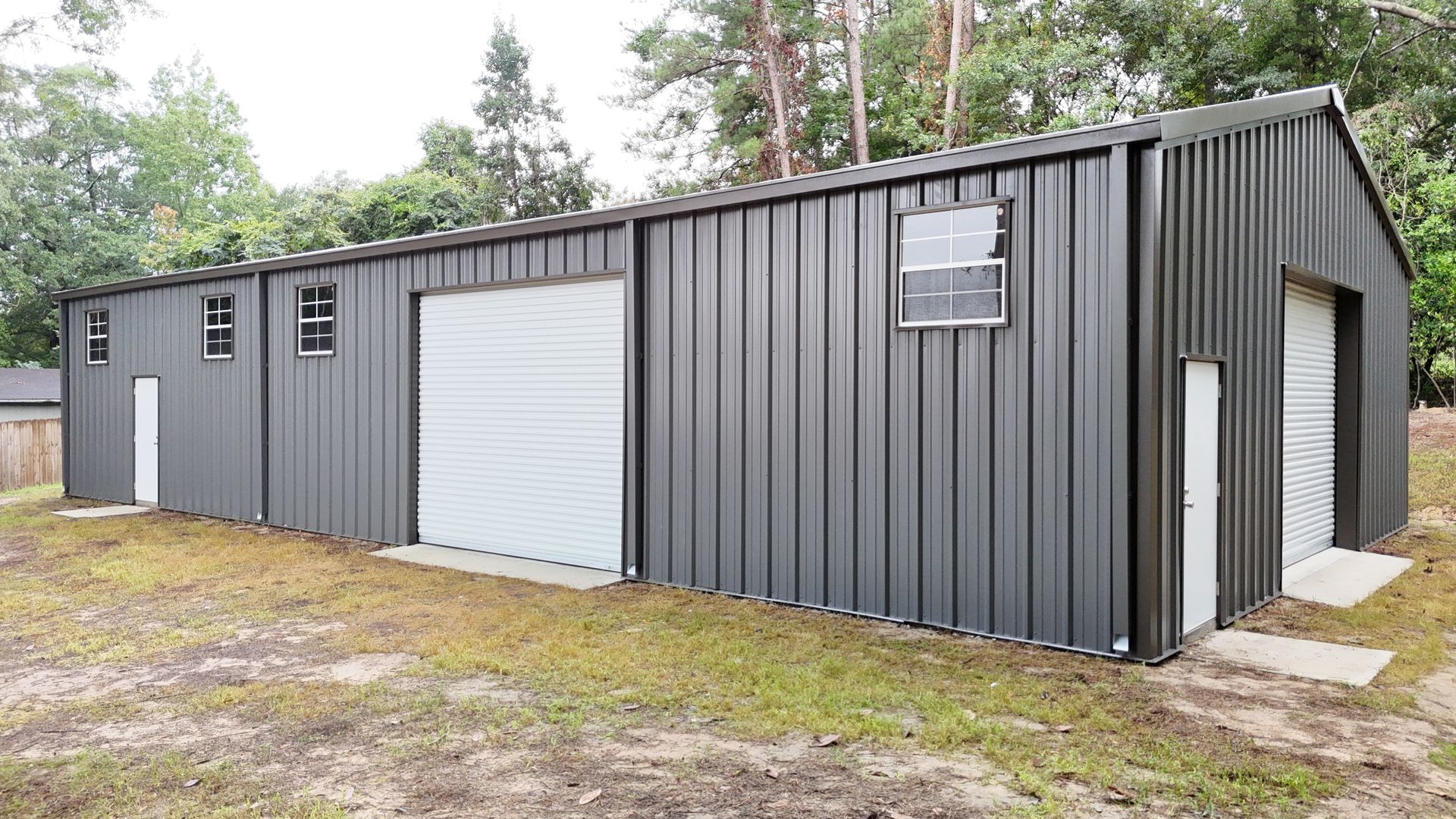 Dark gray metal building with garage doors, windows, and a white door. Located outdoors.