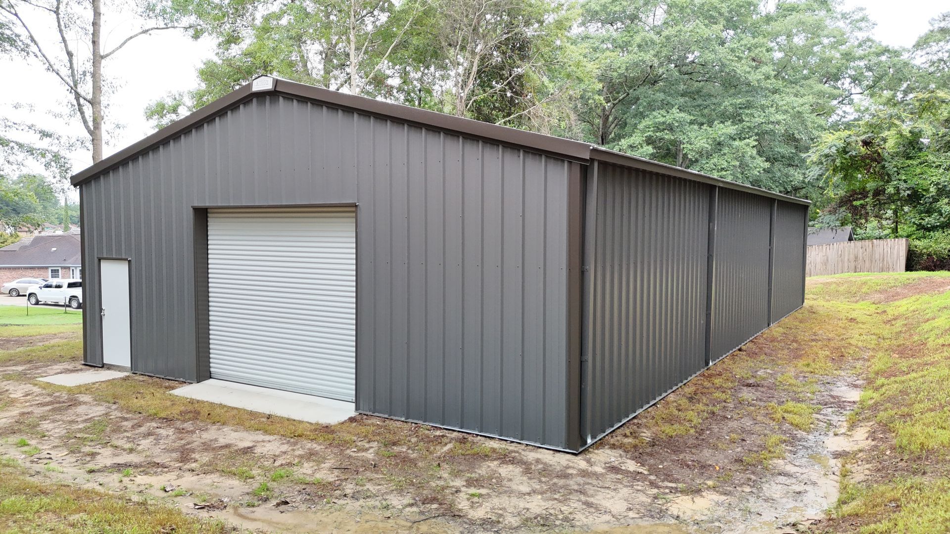 Dark gray metal storage building with a roll-up door and a side door on a grassy lot.