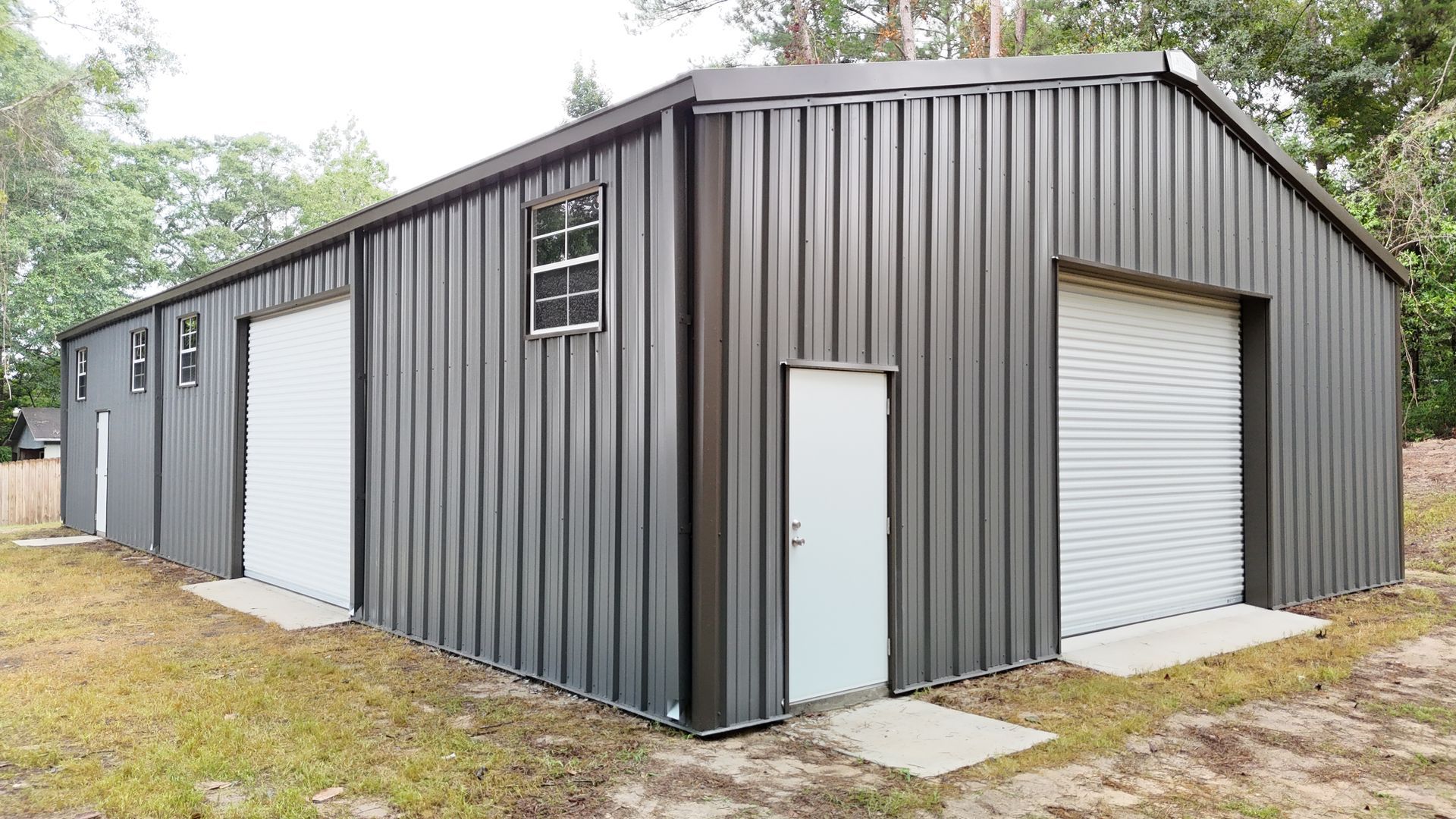 Gray metal warehouse with white doors and a small window, in a grassy outdoor setting.