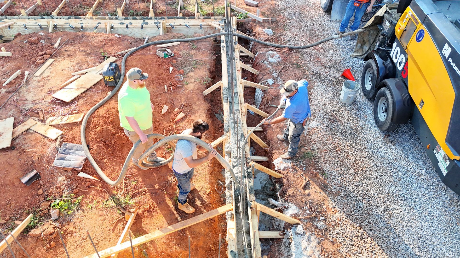 Construction workers pouring concrete into a wooden form using a pump, outdoors.