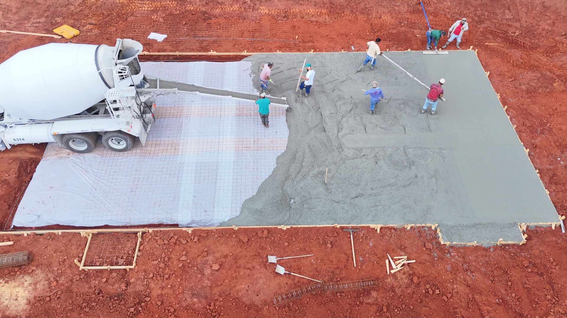 Concrete being poured into a foundation form by a cement truck, with workers leveling the wet cement.
