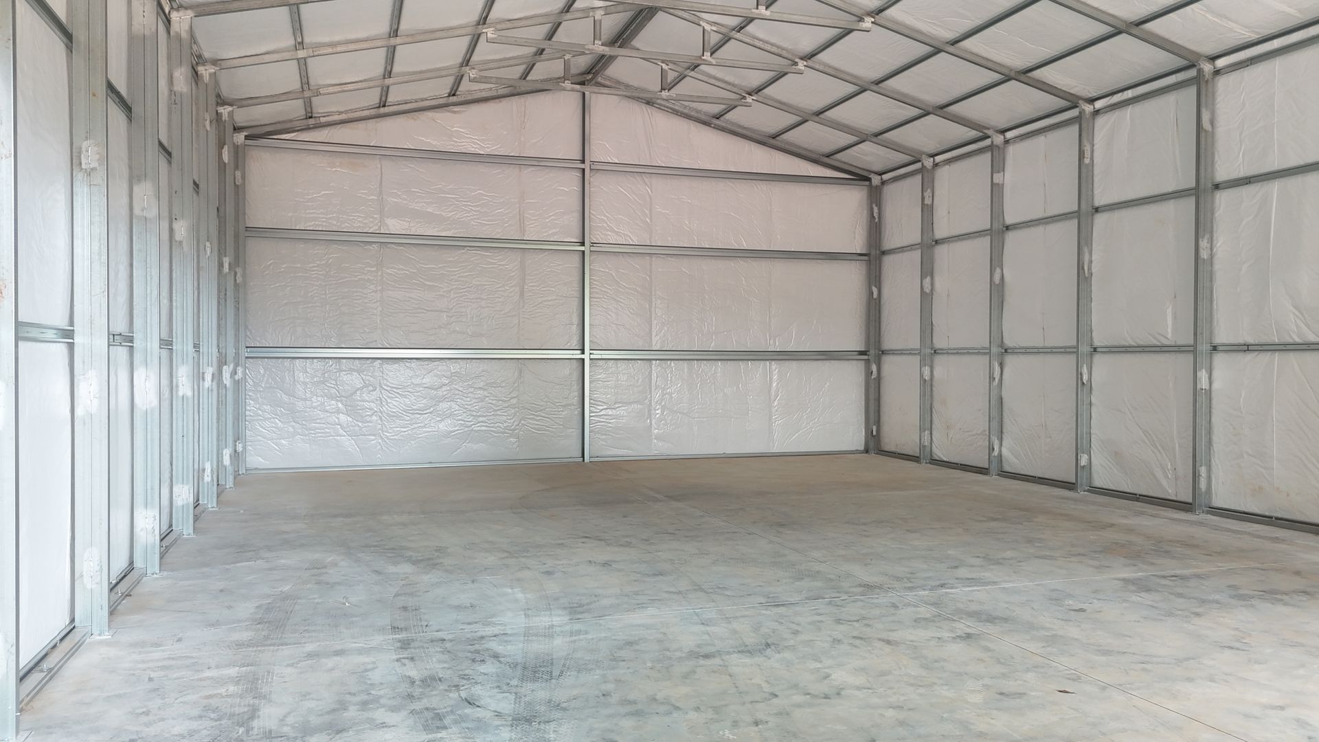Empty, gray-floored metal storage building with white walls and roof supports.