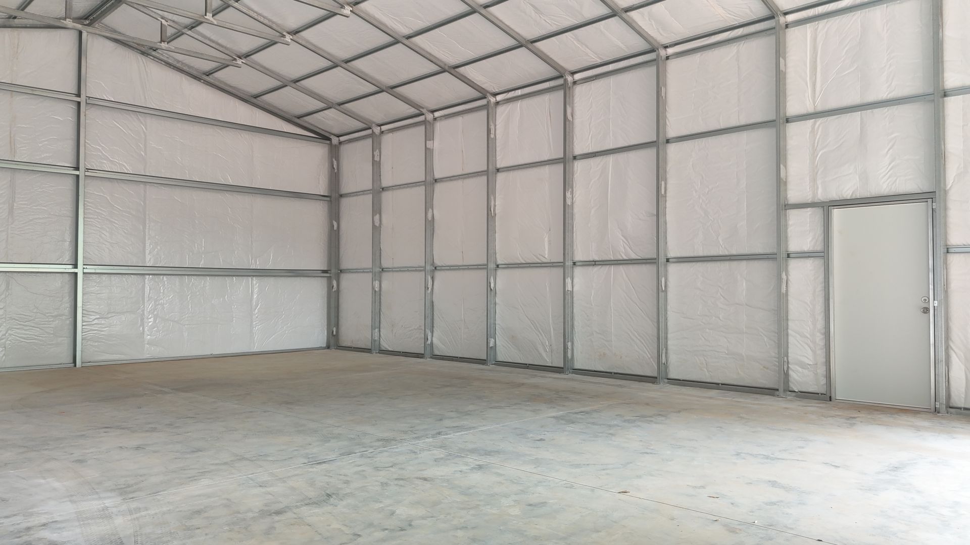 Empty metal frame warehouse interior with concrete floor and a single door.
