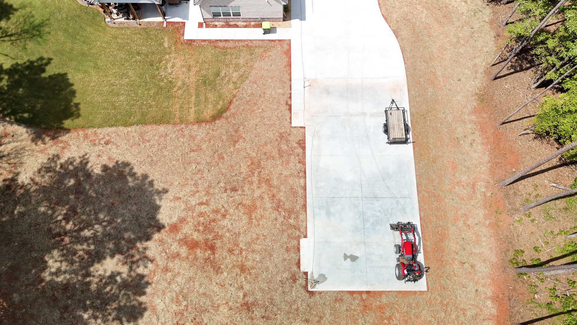 Aerial view: driveway with red and gray vehicles, a house on green grass, and surrounding trees.