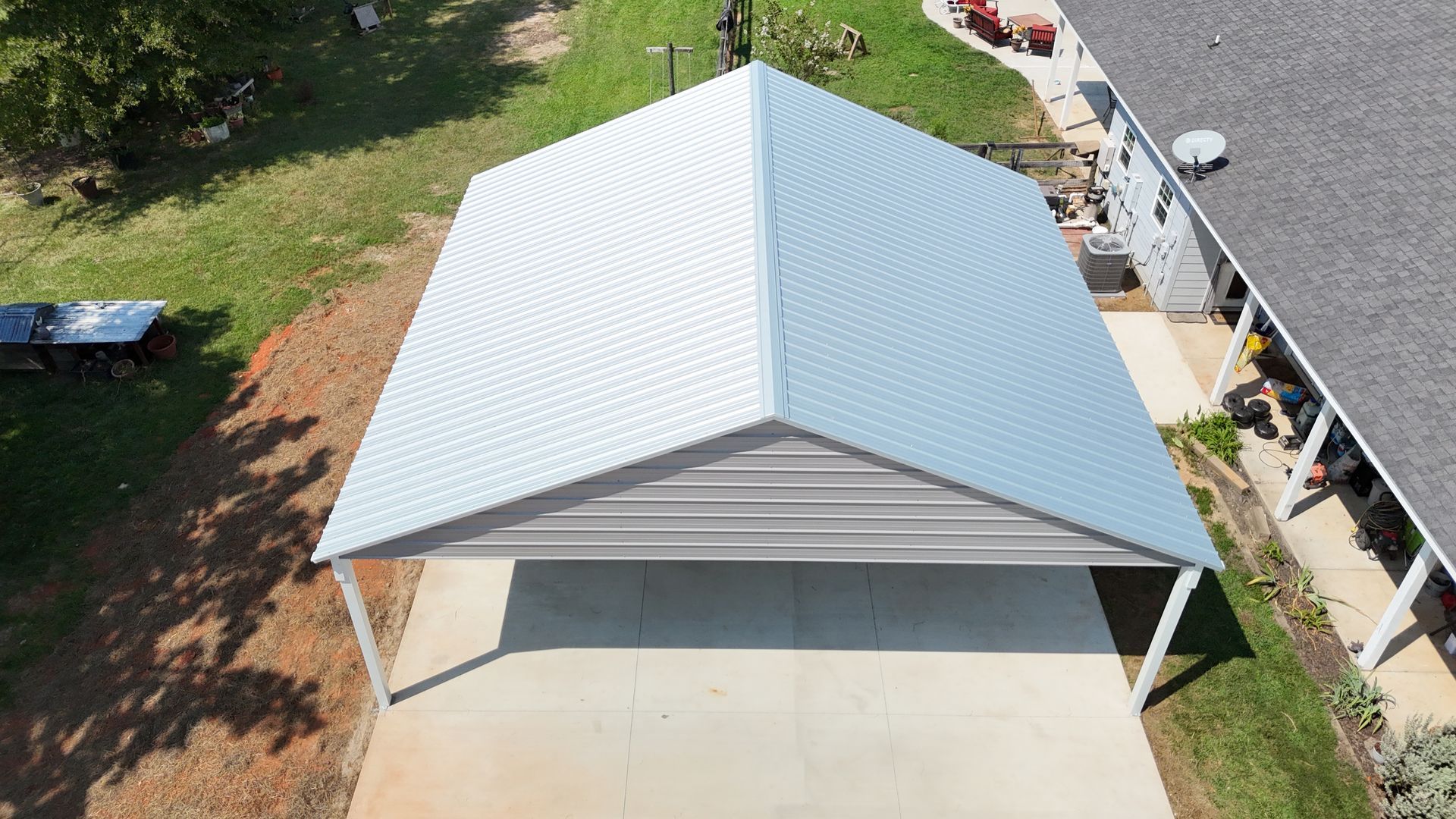 Carport with a white metal roof, on a concrete pad, adjacent to a house and grassy area.