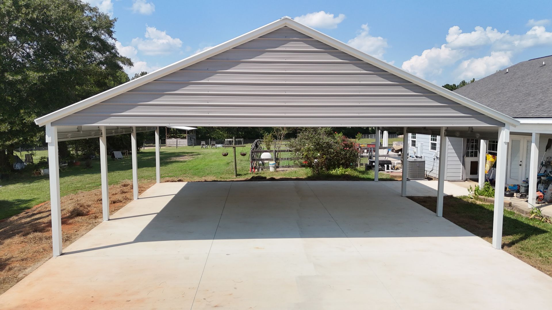 Carport with gray roof over a concrete pad, next to a house.