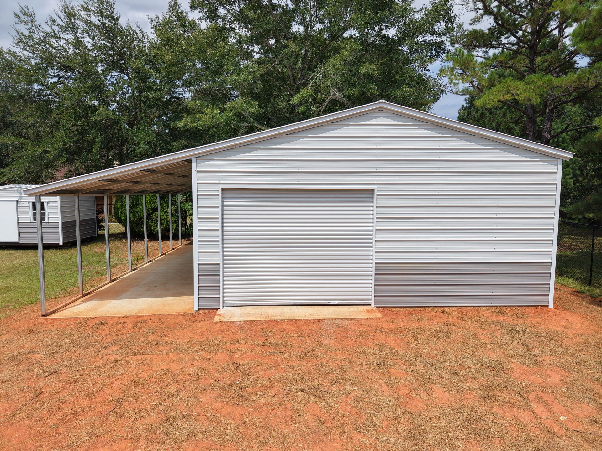 Metal garage with attached carport, white and gray siding, on a red dirt lot.