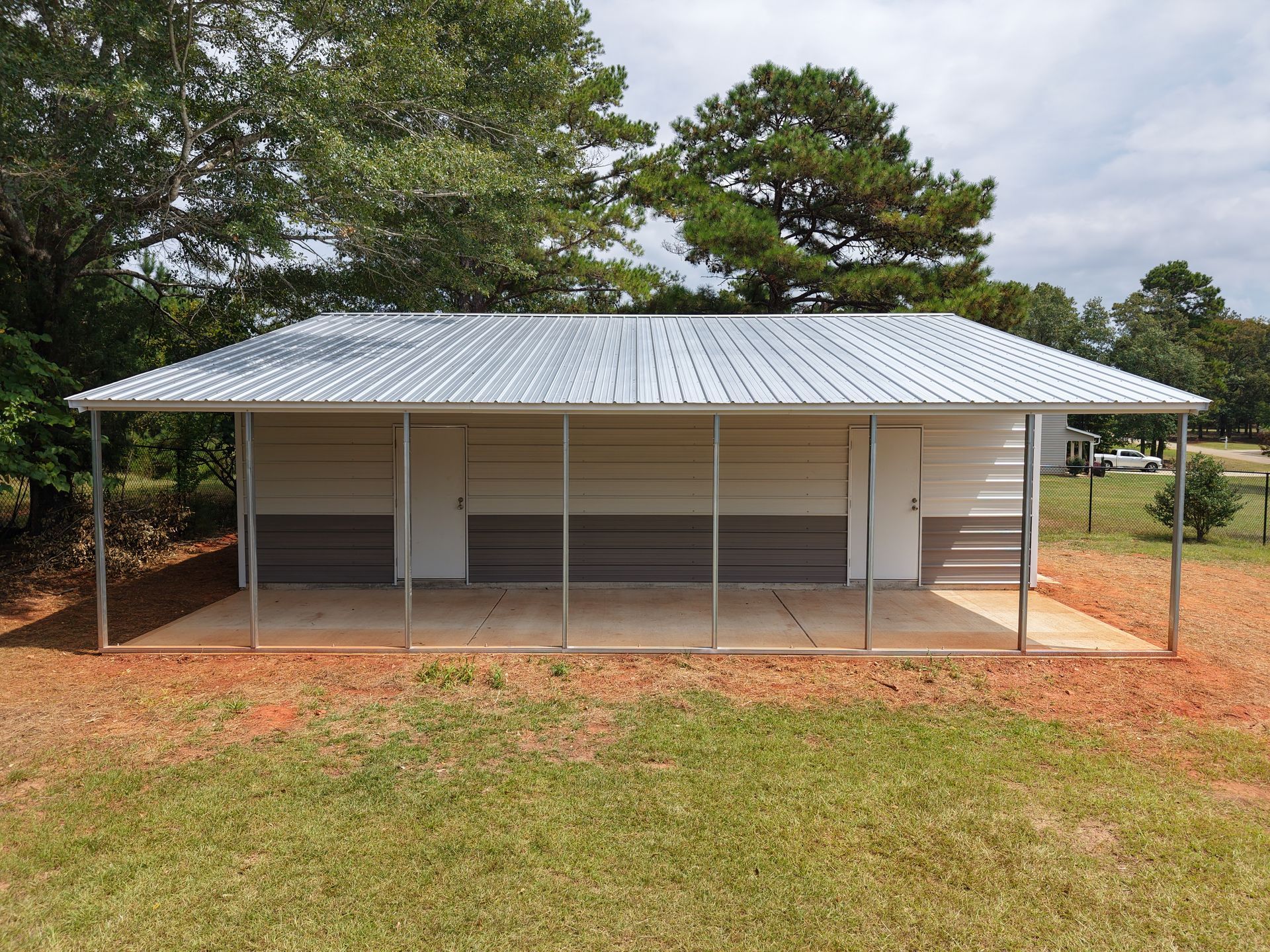A rectangular, open-air public restroom with a metal roof, in a grassy area.