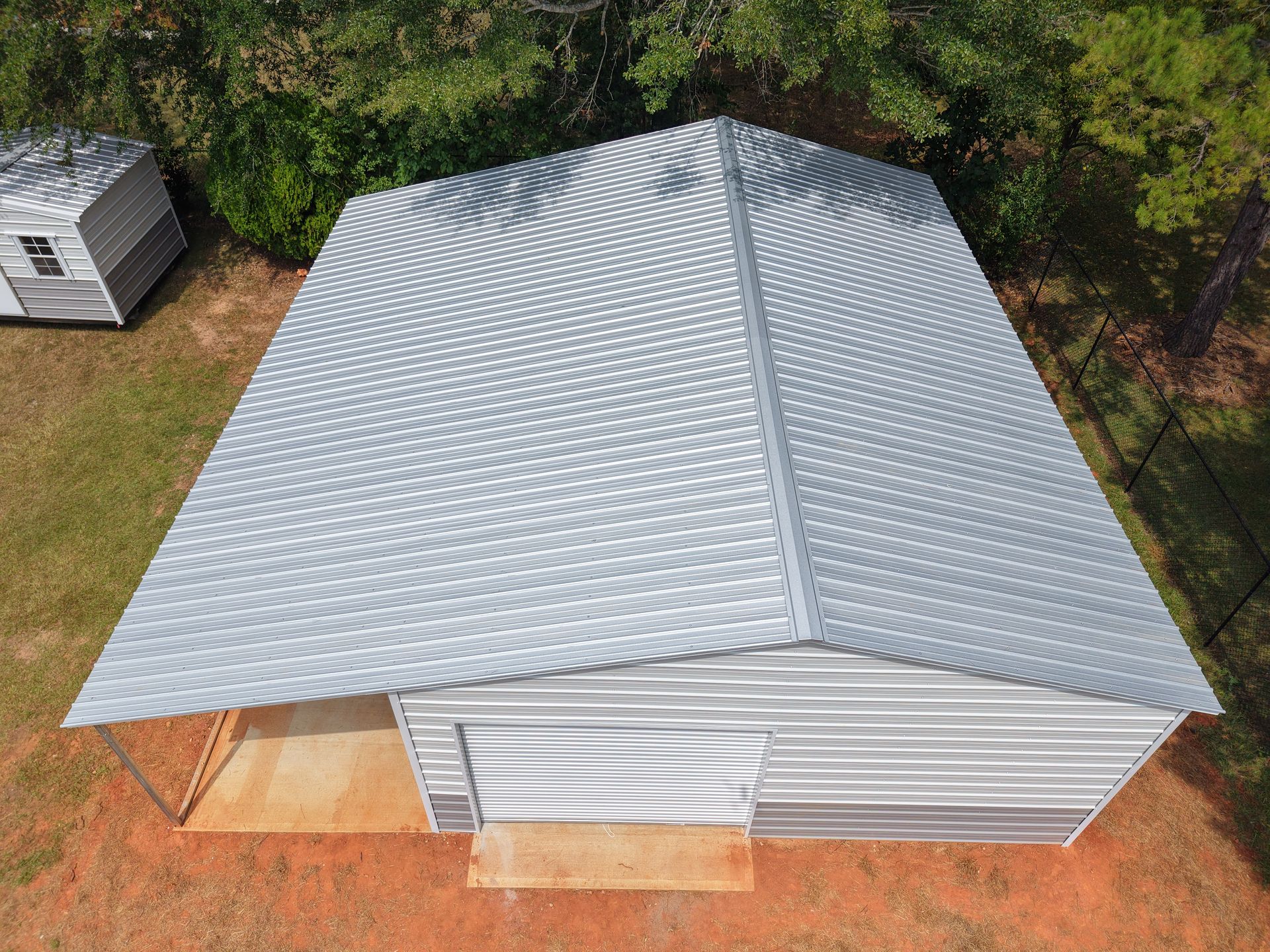 Metal-roofed shed with a lean-to, another shed in the background, and trees.
