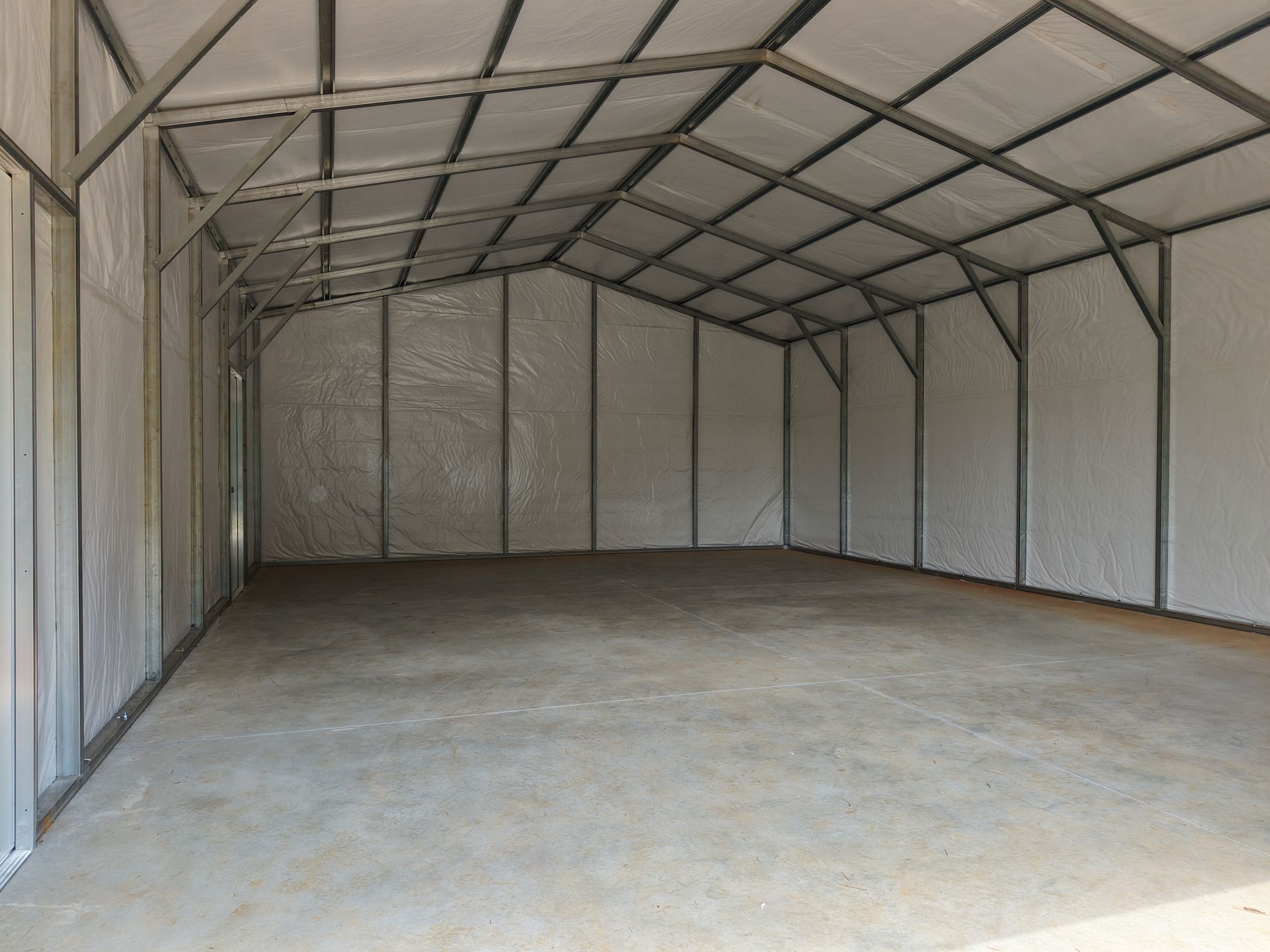 Empty metal storage shed with concrete floor and white walls.