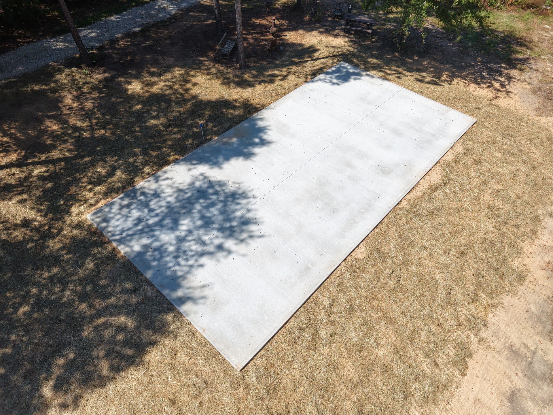 A rectangular concrete slab on dry grass, with a tree shadow cast across it.