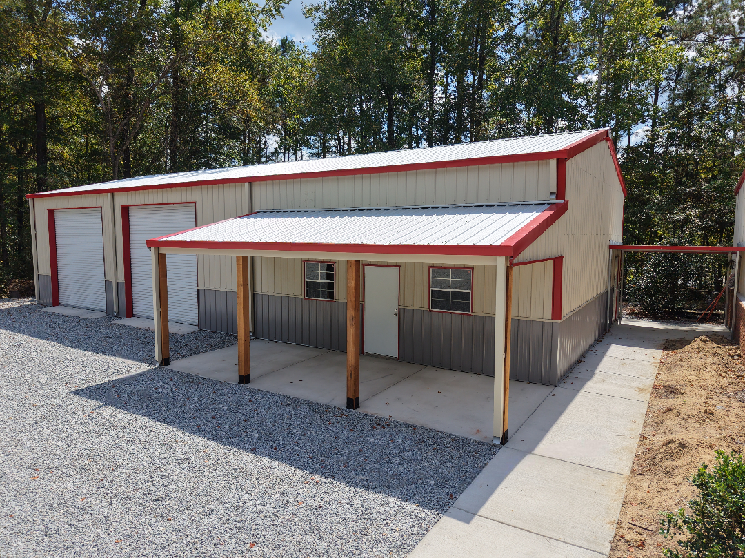 Tan metal building with red trim, two garage doors, and a covered porch. Gravel driveway.