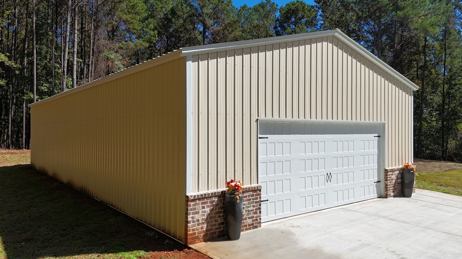 Beige metal building with white garage door, brick accents, and trees in the background.